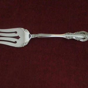 Pode incluir: Um garfo de prata com um cabo ornamentado e um design decorativo. O garfo tem três dentes e uma borda arredondada.