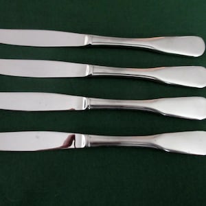 May include: Four silver dinner knives with smooth, rounded handles.