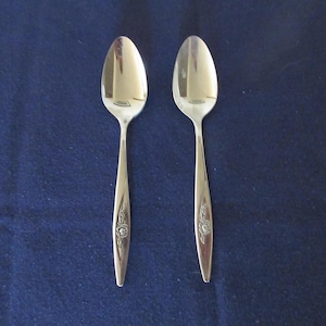 May include: Two silver teaspoons with floral designs on a blue background.