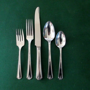 May include: A set of five silver-plated flatware pieces, including a knife, two forks, and two spoons, arranged on a green surface.