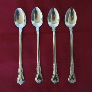 May include: Four silver spoons with ornate handles are arranged on a deep red background. The spoons have a classic design, with a long, slender handle and a rounded bowl. The handles feature a decorative floral pattern.