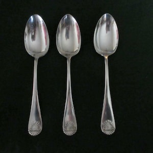 May include: Three silver spoons with oval bowls and long, slender handles. Each spoon has a decorative shell design at the base of the handle. The spoons are arranged vertically against a dark background.