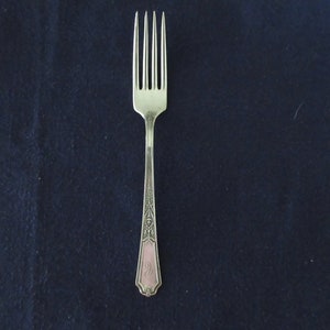 May include: A silver fork with an ornate design and a pink monogram on the handle.
