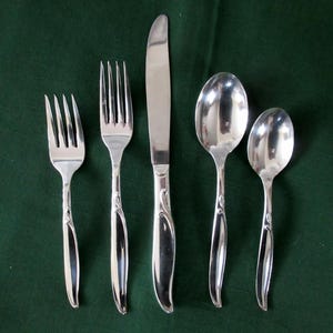 May include: A set of five silver-plated cutlery pieces, including a knife, two forks, and two spoons. The pieces have an ornate design with a floral motif.