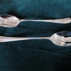May include: A set of two silver serving utensils, one a spoon and the other a fork, on a green background.