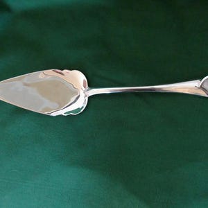 Può includere: Un server per torte argentato con manico a forma di cuore e lama triangolare. Il server è realizzato in metallo lucido ed è progettato per servire torte o crostate. Il manico ha un design a forma di cuore all'estremità.