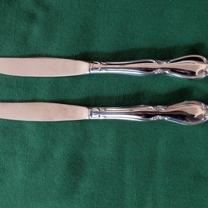 May include: Two silver dinner knives with ornate handles on a green background.