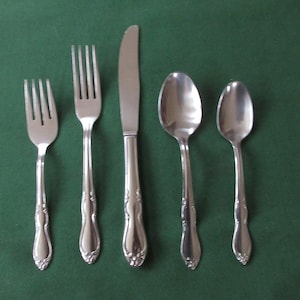 Può includere: Un set di cinque posate argentate, tra cui un coltello, due forchette e due cucchiai. I pezzi hanno manici decorati con un motivo floreale.
