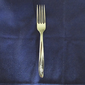 May include: A silver fork with a floral design on the handle. The fork is on a blue background.