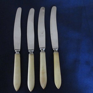 May include: Four silver butter knives with ivory-colored handles. The knives have a simple, classic design.