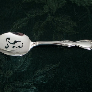 Può includere: Un cucchiaio da portata in argento con un design decorativo tagliato. Il cucchiaio ha una ciotola arrotondata e un manico lungo con un motivo floreale.