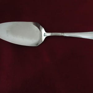 May include: A silver cake server with a decorative handle. The handle has a floral design and a raised edge.