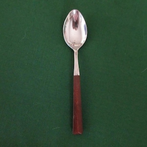 May include: A silver spoon with a polished, oval bowl and a dark brown wooden handle. The spoon is set against a dark green background, highlighting its simple elegance. A classic utensil for serving.