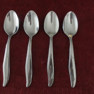 May include: Four silver teaspoons with a star design on the handle. The spoons are arranged in a row on a red surface.