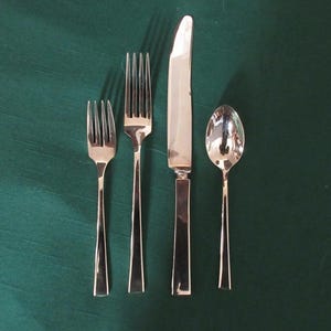 May include: A set of silverware on a green tablecloth. The set includes a knife, a fork, and a spoon.