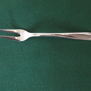 May include: A silver cocktail fork with two prongs on a green surface.