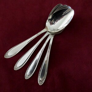 May include: Five silver spoons stacked on top of each other on a burgundy background.