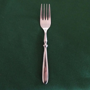 May include: A silver fork with four tines, set against a dark green background. The fork has a decorative handle with a rounded base. This utensil is suitable for dining.