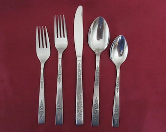 May include: A set of five silver-colored flatware pieces arranged on a red background. The set includes two forks, a knife, and two spoons. Each piece has a decorative floral pattern on the handle.