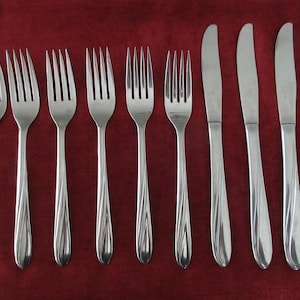 May include: A set of stainless steel forks and knives arranged on a deep red background. The forks have four tines and a decorative handle. The knives have a smooth, curved blade and a matching handle. The silverware is designed for dining.