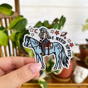 May include: A sticker featuring a cartoon woman riding a blue horse with the text "I NEED SPACE" and stars and a planet in the background.