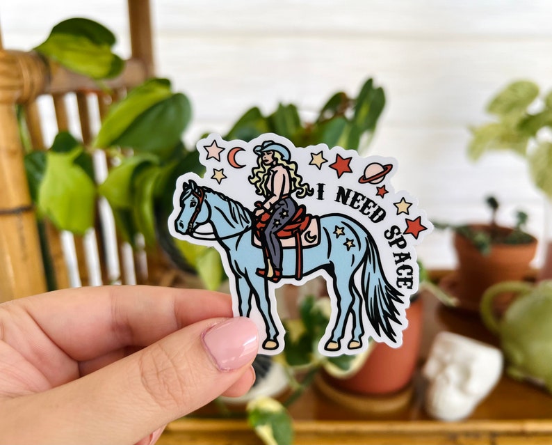 May include: A sticker featuring a cartoon woman riding a blue horse with the text "I NEED SPACE" and stars and a planet in the background.