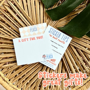 K&ouml;nnte beinhalten: Zwei Karten mit einem Pfirsich-Design. Die obere Karte hat ein Pfirsich-Muster und lautet "Feel Like a Peach". Die untere Karte sagt "A Gift For You!" und hat einen Pfirsich-Aufkleber mit dem Text "Feel Like a Peach" und "New Stickers!" Die Karten liegen auf einer geflochtenen Weidenoberfl&auml;che mit einem gr&uuml;nen Blatt.