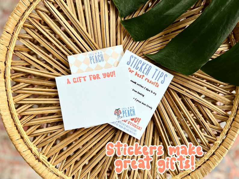 Pode incluir: Dois cart&otilde;es com um design de p&ecirc;ssego. O cart&atilde;o superior tem um padr&atilde;o de p&ecirc;ssego e diz "Feel Like a Peach". O cart&atilde;o inferior diz "A Gift For You!" e tem um adesivo de p&ecirc;ssego com o texto "Feel Like a Peach" e "New Stickers!" Os cart&otilde;es est&atilde;o sobre uma superf&iacute;cie de vime tran&ccedil;ado com uma folha verde.