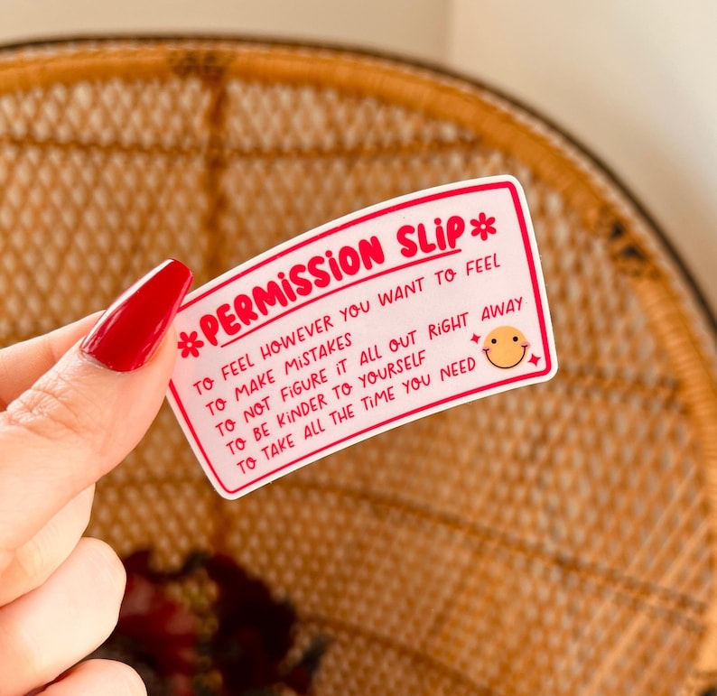 Puede incluir: Una pegatina blanca con texto rosa que dice "*PERMISSION SLIP* TO FEEL HOWEVER YOU WANT TO FEEL TO MAKE MISTAKES TO NOT FIGURE IT ALL OUT RIGHT AWAY TO BE KINDER TO YOURSELF TO TAKE ALL THE TIME YOU NEED". Una carita sonriente est&aacute; en la esquina inferior derecha.