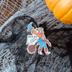 K&ouml;nnte beinhalten: Ein Aufkleber mit einer Comic-Hexe mit blonden Haaren, die einen blauen Hut und ein rotes Hemd tr&auml;gt und auf einem Besen reitet. Der Text "Let's go Witches" ist in Schwarz auf wei&szlig;em Hintergrund geschrieben.