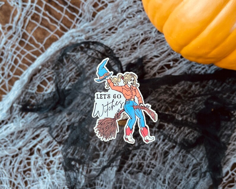 K&ouml;nnte beinhalten: Ein Aufkleber mit einer Comic-Hexe mit blonden Haaren, die einen blauen Hut und ein rotes Hemd tr&auml;gt und auf einem Besen reitet. Der Text "Let's go Witches" ist in Schwarz auf wei&szlig;em Hintergrund geschrieben.