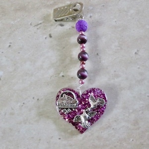 May include: A purple heart-shaped charm with silver doves and glitter. The charm is attached to a purple beaded chain with a silver clip.