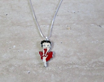 May include: A silver chain necklace with a charm of a cartoon woman in a red dress.