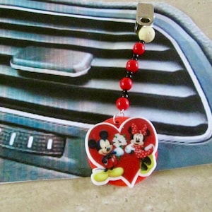 May include: Red heart-shaped car air freshener with a Mickey Mouse, Minnie Mouse, and Goofy design. The air freshener is hanging from a black and red beaded chain.