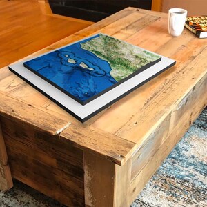 May include: A wooden coffee table with a distressed finish. A framed map of a coastal region is on top of the table.