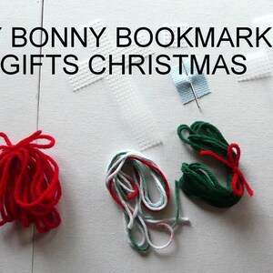 May include: DIY Bonny Bookmarks Gifts Christmas - A close-up of a craft project with white plastic canvas, red, green, and white yarn, and a needle. The yarn is tied into bows and the canvas is cut into cross shapes.