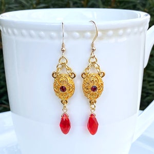 Puede incluir: Pendientes de oro con una piedra preciosa roja y un cristal rojo en forma de lágrima.