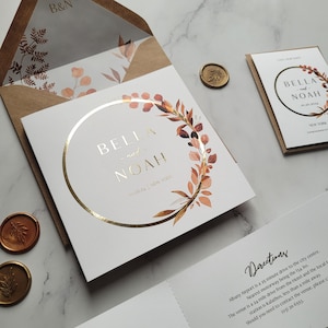 May include: A white wedding invitation with a gold circle and a watercolor floral wreath. The names "Bella and Noah" are written in gold script inside the circle. The date "3.10.24" and the location "New York" are written below the names. The invitation also includes directions to the venue.