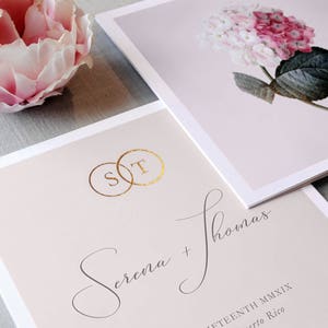 Puede incluir: Una invitación de boda con un diseño floral rosa y blanco. La invitación presenta los nombres de la pareja, "Serena + Thomas", y la fecha "Seventeenth MMXIX".