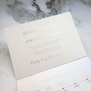 May include: A cream-colored wedding invitation card featuring gold foil lettering. The text reads Renee Winston & Owain Thomas, invite you to celebrate their marriage, Saturday 15th August 2028 at 2pm, Ch&acirc;teau de Saint Loup sur Thouet, Party to follow until late, and Order of the Day.