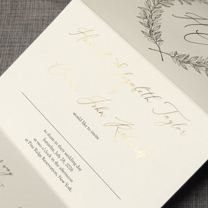 May include: A wedding invitation card featuring gold foil calligraphy text that reads Hannah Elizabeth Taylor and John Richards would like to invite to share in their wedding day Saturday, July 28, 2026 at two o'clock at Pine Ridge Reservation.