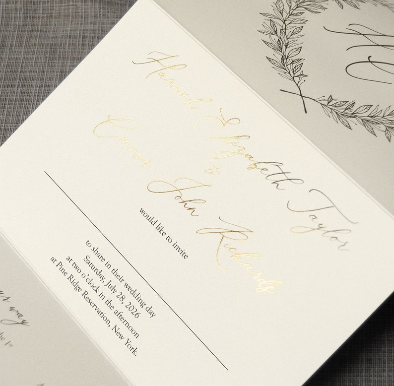 May include: A wedding invitation card featuring gold foil calligraphy text that reads Hannah Elizabeth Taylor and John Richards would like to invite to share in their wedding day Saturday, July 28, 2026 at two o'clock at Pine Ridge Reservation.