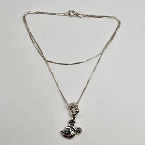 May include: A silver necklace featuring a Mickey Mouse pendant. The pendant has a black stone design for the ears and a silver face. The necklace chain is a delicate box chain style.