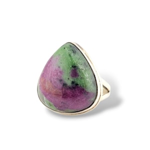 May include: A ring featuring a large, pear-shaped cabochon stone with a smooth, polished surface. The stone displays a marbled pattern of vibrant magenta-pink and deep forest green colors with small black inclusions, set in a simple silver band.