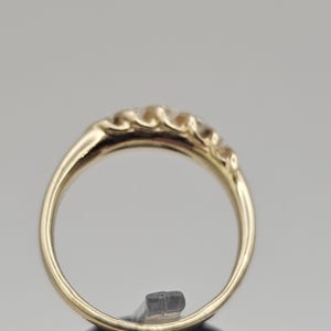 Puede incluir: Un anillo de oro con una serie de peque&ntilde;as piedras preciosas transparentes en la parte superior. La banda del anillo es de oro pulido. Las piedras preciosas est&aacute;n espaciadas uniformemente y a&ntilde;aden un toque de brillo.