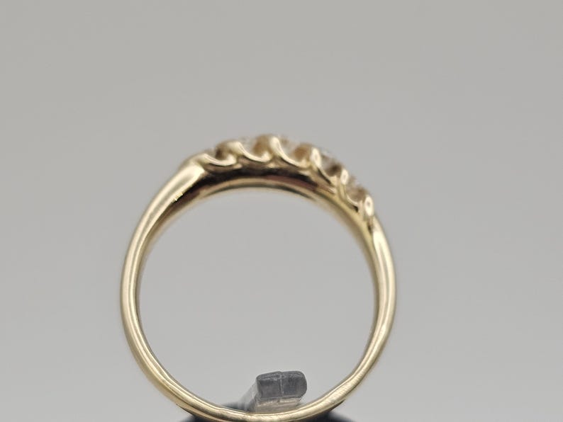 Puede incluir: Un anillo de oro con una serie de peque&ntilde;as piedras preciosas transparentes en la parte superior. La banda del anillo es de oro pulido. Las piedras preciosas est&aacute;n espaciadas uniformemente y a&ntilde;aden un toque de brillo.