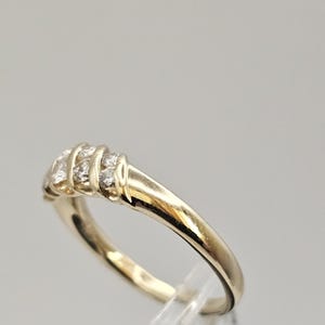 Puede incluir: Un anillo dorado con una serie de peque&ntilde;as piedras preciosas transparentes. El anillo tiene una banda lisa y pulida y una secci&oacute;n superior decorativa con las piedras preciosas. El anillo es probablemente de oro.