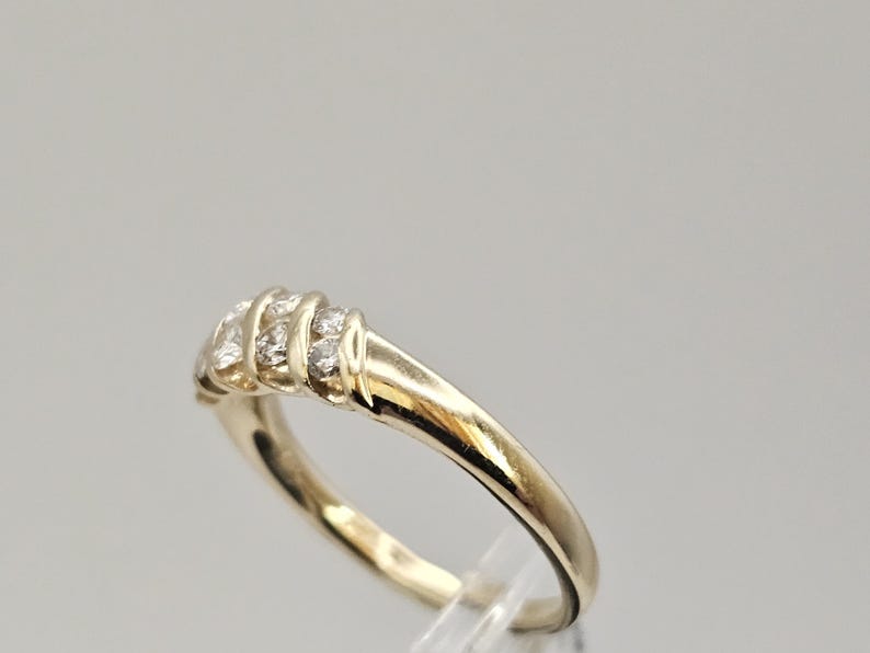Puede incluir: Un anillo dorado con una serie de peque&ntilde;as piedras preciosas transparentes. El anillo tiene una banda lisa y pulida y una secci&oacute;n superior decorativa con las piedras preciosas. El anillo es probablemente de oro.