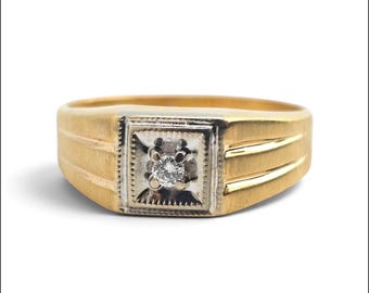 May include: A gold ring featuring a brushed finish on the band and a square-shaped white metal setting at the center. The setting contains a single round brilliant-cut clear gemstone held in place by four prongs, surrounded by a decorative border.