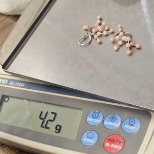 May include: A pair of earrings with pink beads and silver-colored metal components rests on a silver scale. The scale displays a weight of 4.2 grams. The earrings have a cluster design, with multiple small pink beads.